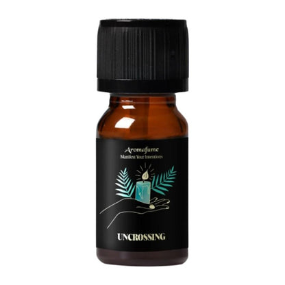 A small amber glass bottle with a black ribbed cap and a black label. The label features a teal candle illustration with palm leaves and the text 'Aromafume', 'Manifest your intentions', and 'UNCROSSING'.