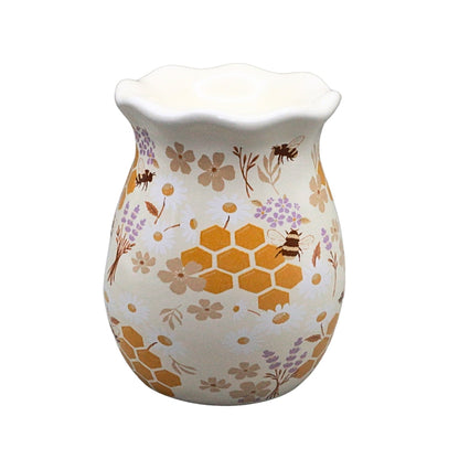 A ceramic wax warmer with a scalloped rim, decorated with a pattern of orange honeycombs, purple flowers, and brown bees on a cream-colored background.
