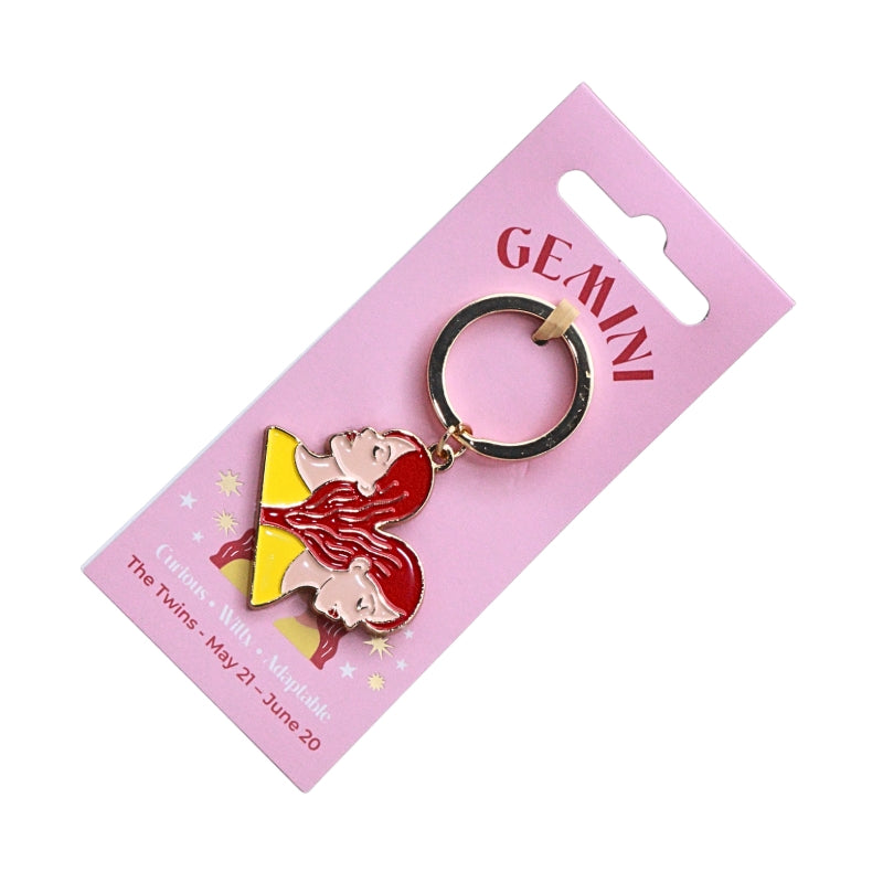 A Gemini-themed keychain featuring two cartoon twin characters in red and yellow, attached to a black split ring and mounted on a pink card labeled GEMINI.