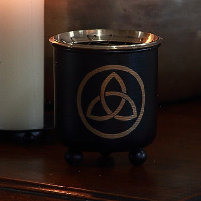 Black and gold incense charcoal burner  with a triquetra  pattern on front on wooden table 