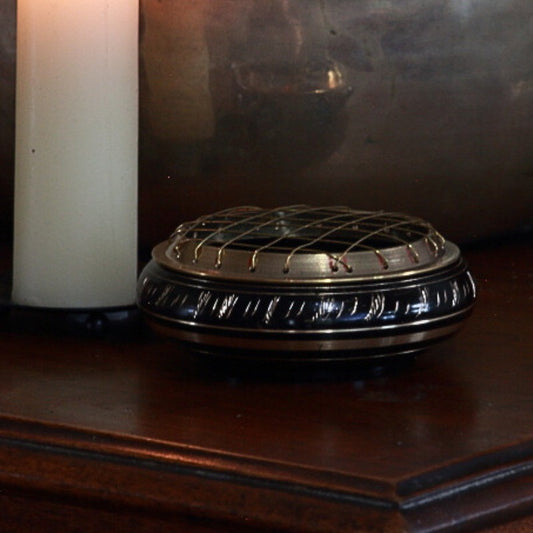 black and gold charcoal incense burner on a wooden table in front of a beeswax candle