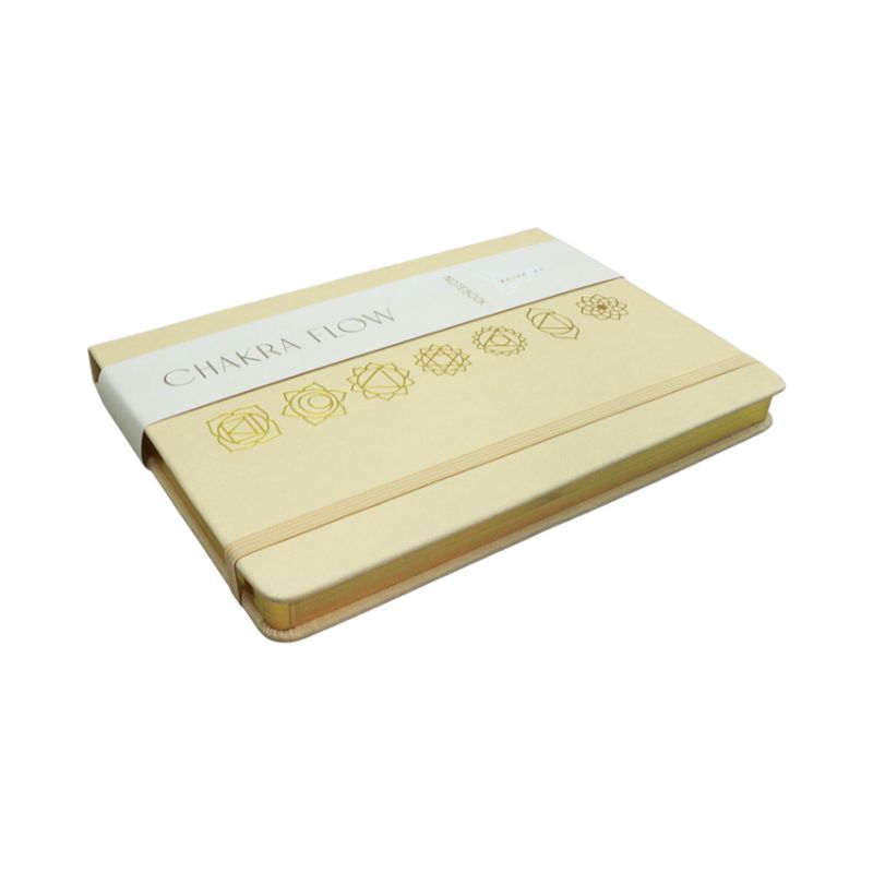 linen cover diary with the chakra symbols printed in gold on the cover. Gold edged pages and a tag with the words "Chakra Flow" and "Notebook" covering it.