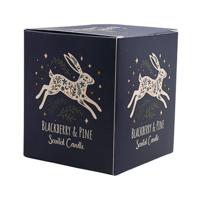 A square navy blue scented candle box with white rabbit illustrations decorated with green leaves and gold stars, labeled 'Blackberry & Pine Scented Candle'.