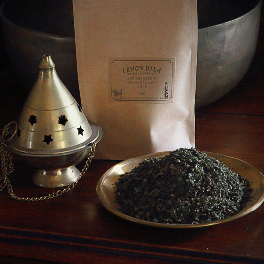 bag of dried herbs on a wooden counter next to a bras censer and plate of dried herbs