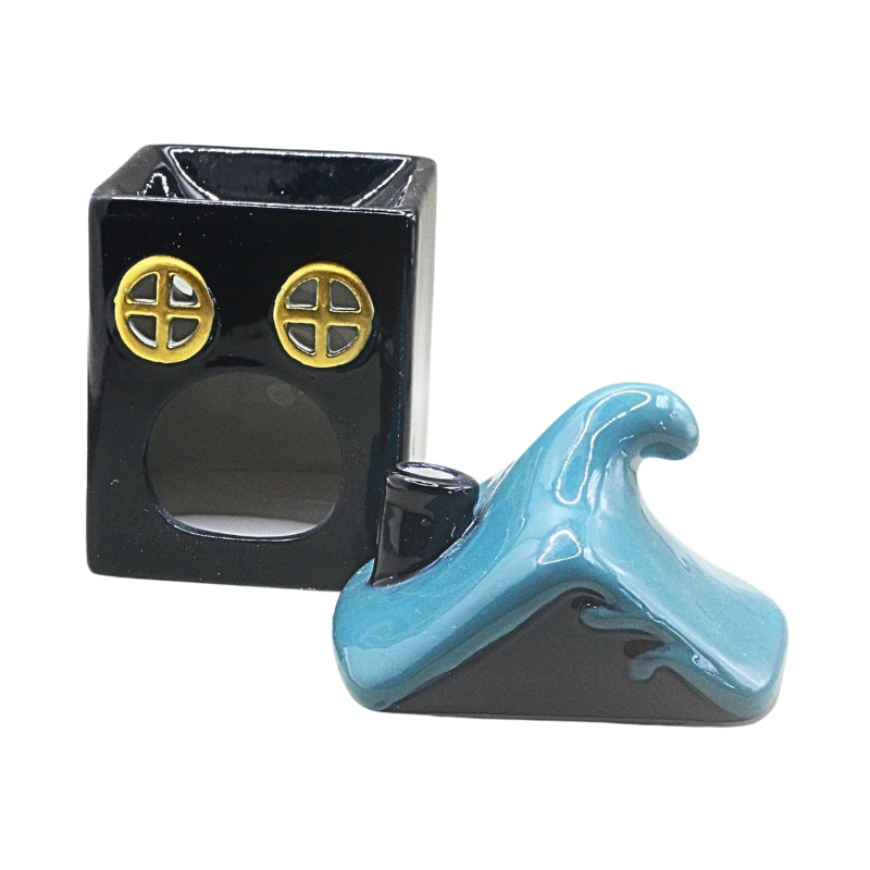 A small glossy ceramic figurine of a  dark blue square house with two round gold window details, shown next to its light and  dark blue wave-shaped lid on a plain white background.