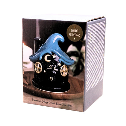 A collectible ceramic witch cottage home candle holder in dark blue and blue, shown inside its original retail packaging box against a white background.