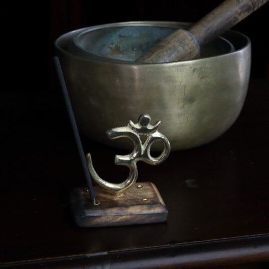 Brass Om Incense Holder On Wooden Stand in front of metal singing bowls