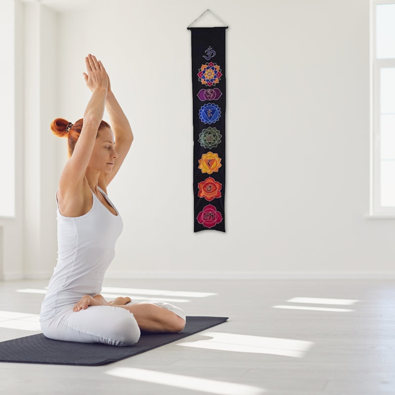 woman practicing yoga in front of a wall banner that has the 7 chakras printed on it