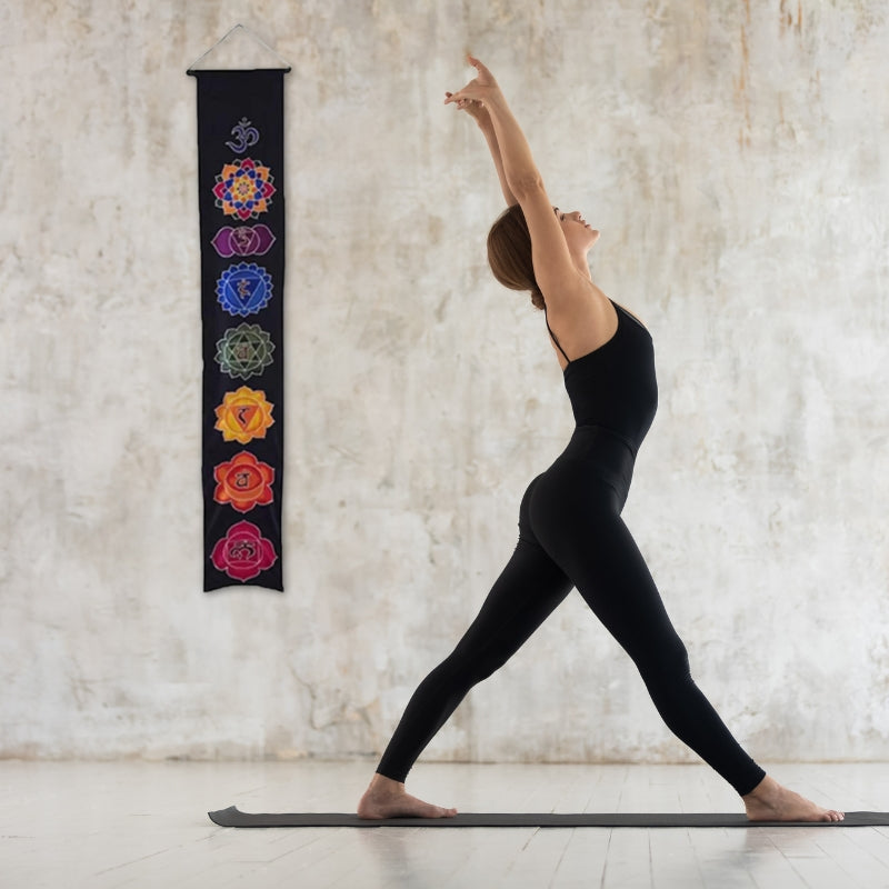 woman practicing yoga in front of a wall banner that has the 7 chakras printed on it