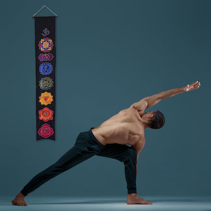man practicing yoga in front of a wall banner that has the 7 chakras printed on it