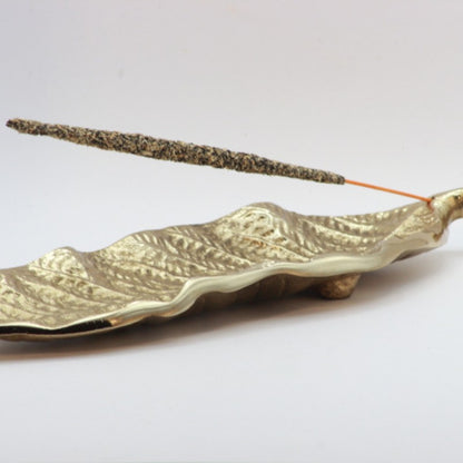 gold incense holder in the shape of a leaf holding a natural incense stick