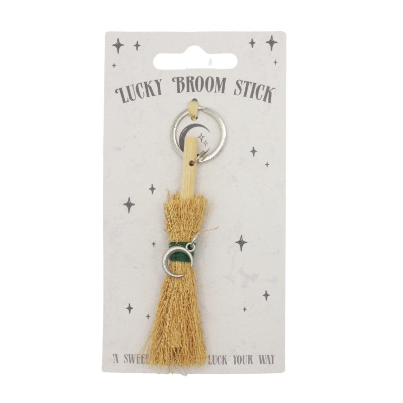 tiny broomstick, with a green string and a crescent moon charm attached to it on a silver keyring