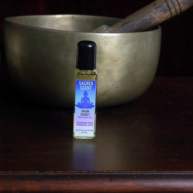 Bottle of Sacred Scents Perfume Oil sitting on a wooden apothecary cabinet in front of a brass singing bowl