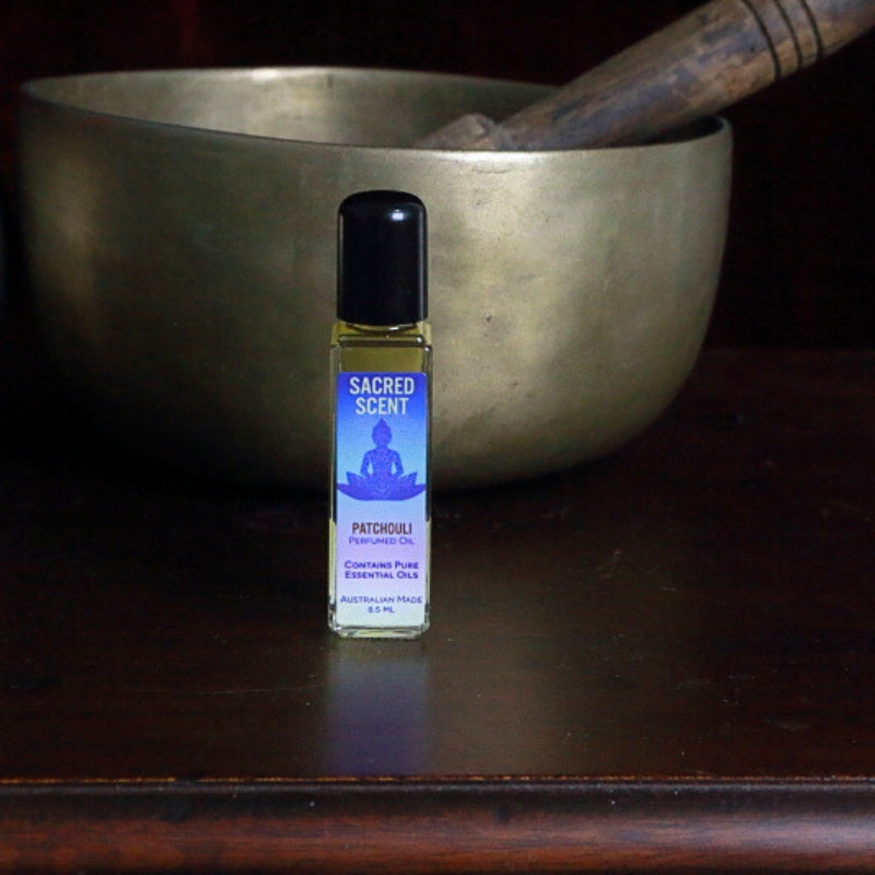 Bottle of Sacred Scents Perfume Oil sitting on a wooden apothecary cabinet in front of a brass singing bowl