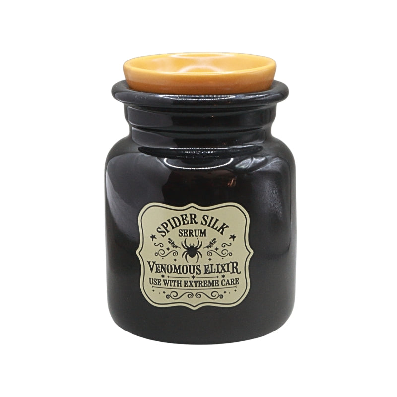 A dark ceramic oil burner  with a black body, a light brown lid, and a vintage-style cream label reading 'Spider Silk Serum' and 'Venomous Elixir'.