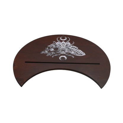 A dark brown wooden half-circular stand featuring an intricate silver-toned engraved moth and moon design on the top surface, with a horizontal slot cut through the center, shown against a plain white background.