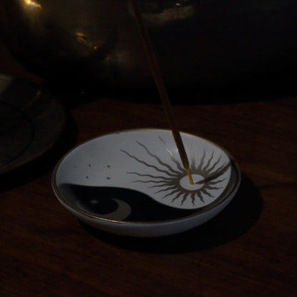 Incense stick in a dish with yin and yang design on a dark background