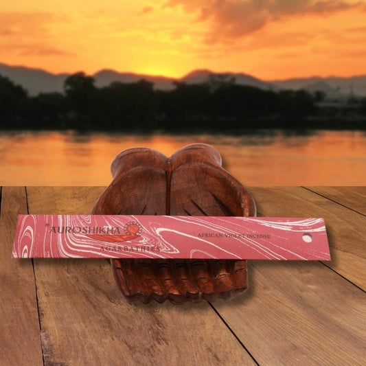 pk of auroshikha incense sitting on a carved wooden hand on a jetty, in front of a golden sunset