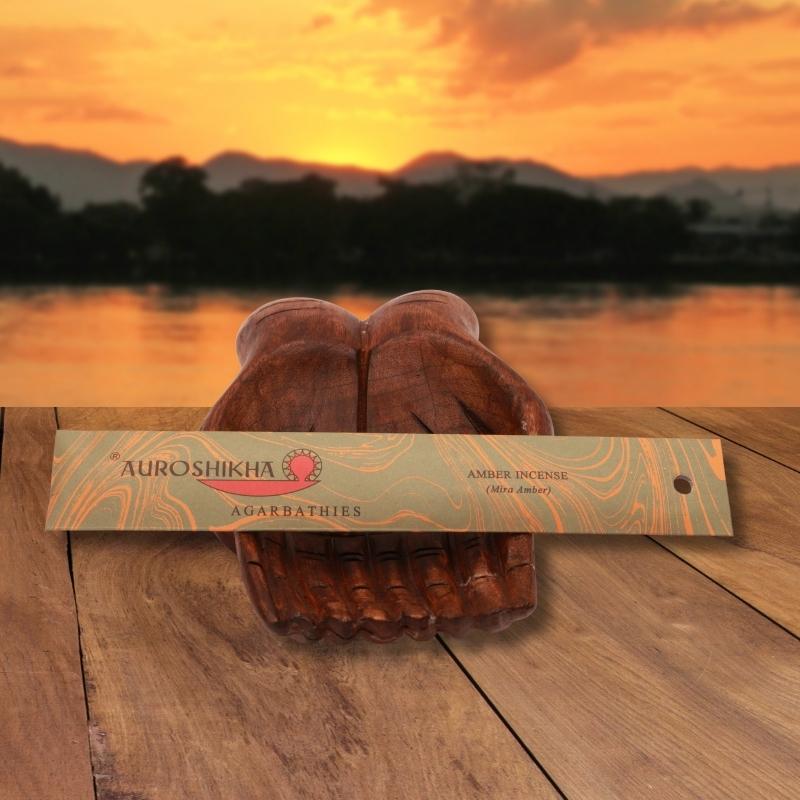 pk of auroshikha incense sitting on a carved wooden hand on a jetty, in front of a golden sunset