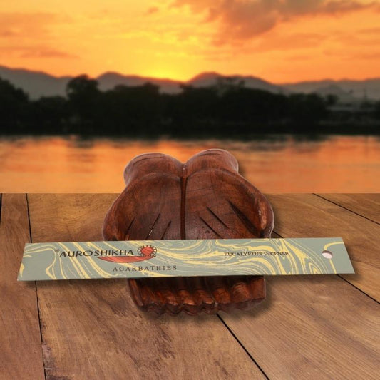 pk of auroshikha incense sitting on a carved wooden hand on a jetty, in front of a golden sunset