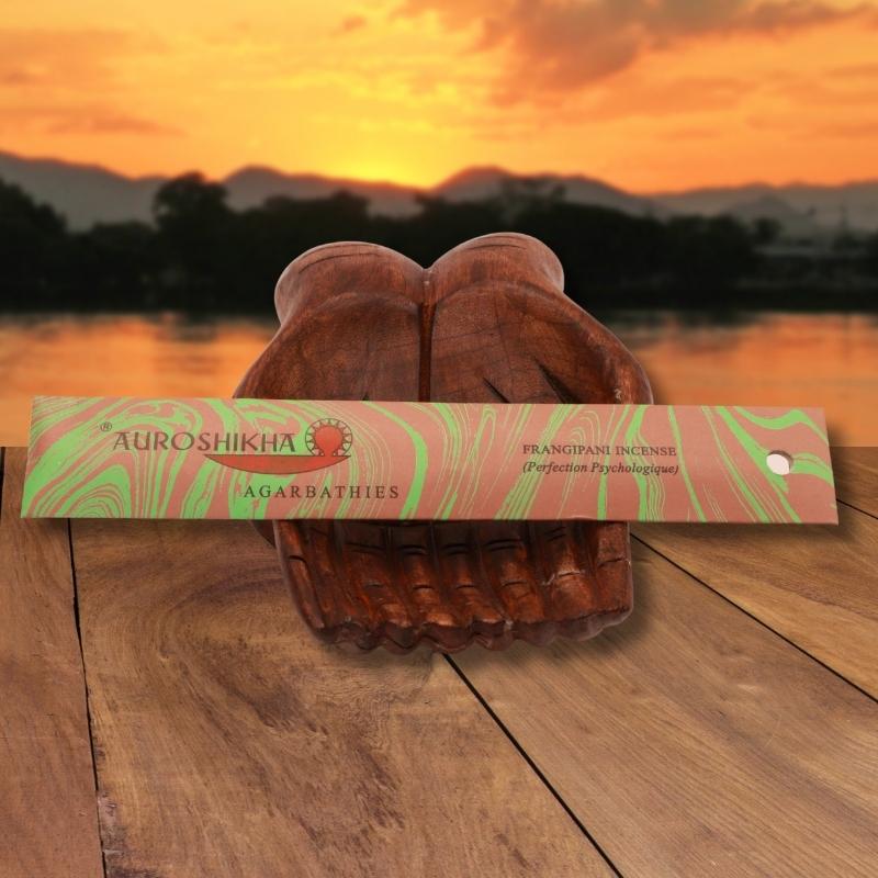 pk of auroshikha incense sitting on a carved wooden hand on a jetty, in front of a golden sunset