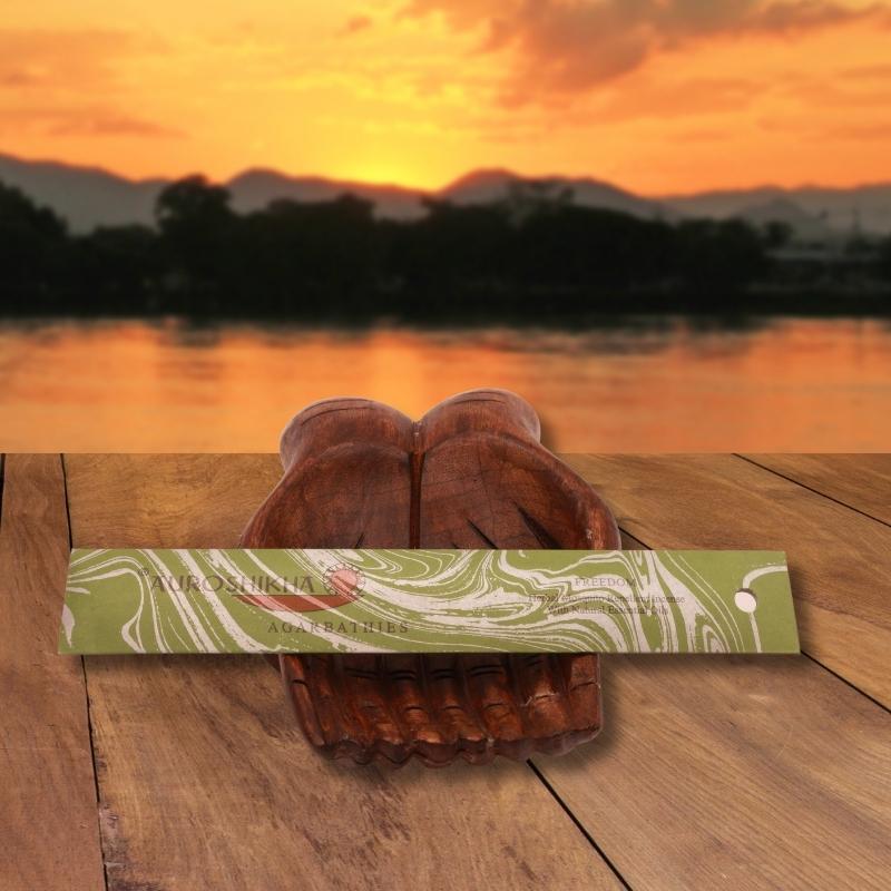 pk of auroshikha incense sitting on a carved wooden hand on a jetty, in front of a golden sunset