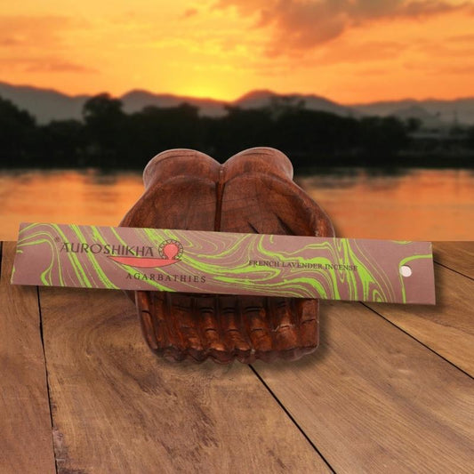 pk of auroshikha incense sitting on a carved wooden hand on a jetty, in front of a golden sunset