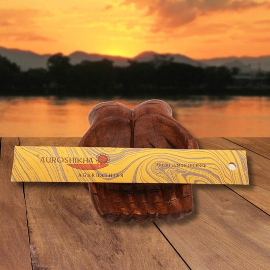 pk of auroshikha incense sitting on a carved wooden hand on a jetty, in front of a golden sunset