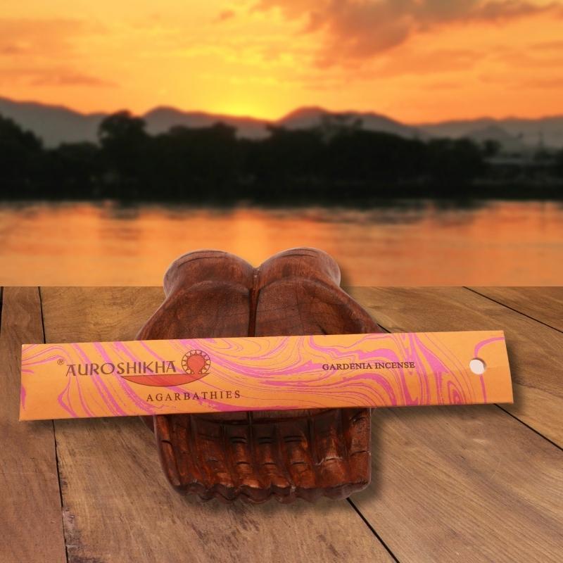 pk of auroshikha incense sitting on a carved wooden hand on a jetty, in front of a golden sunset