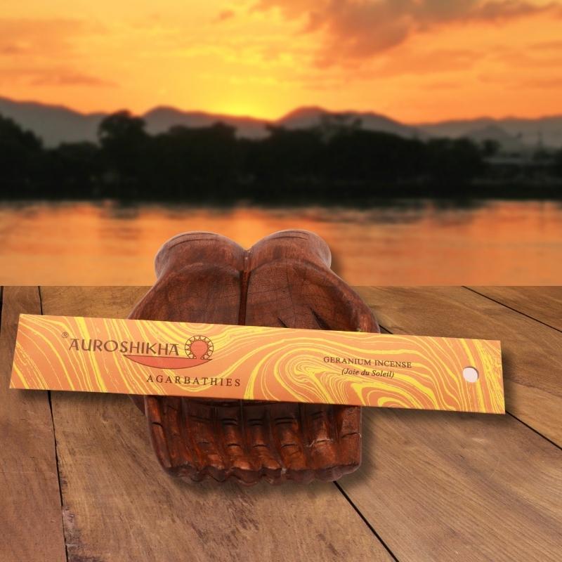 pk of auroshikha incense sitting on a carved wooden hand on a jetty, in front of a golden sunset