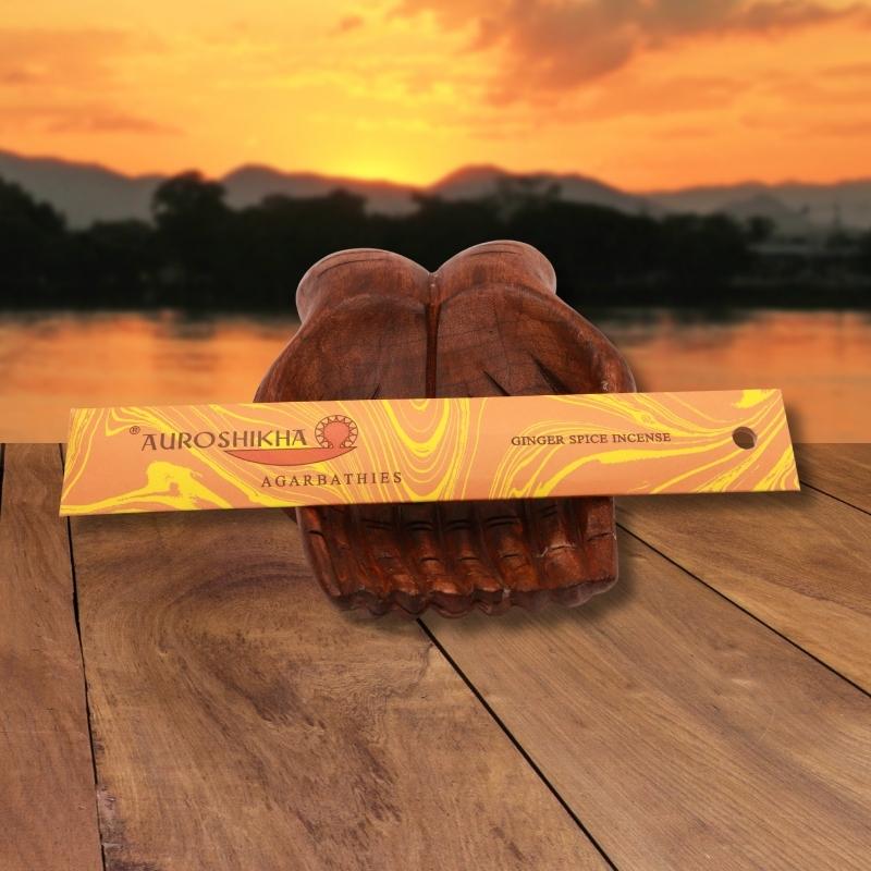 pk of auroshikha incense sitting on a carved wooden hand on a jetty, in front of a golden sunset