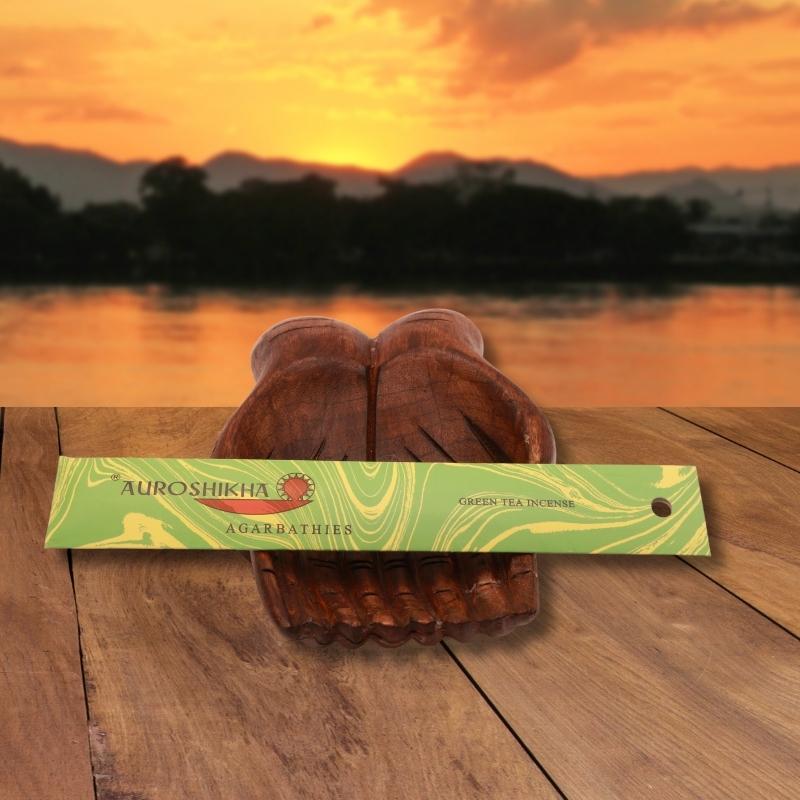 pk of auroshikha incense sitting on a carved wooden hand on a jetty, in front of a golden sunset