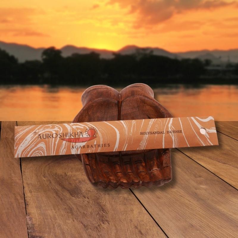 pk of auroshikha incense sitting on a carved wooden hand on a jetty, in front of a golden sunset