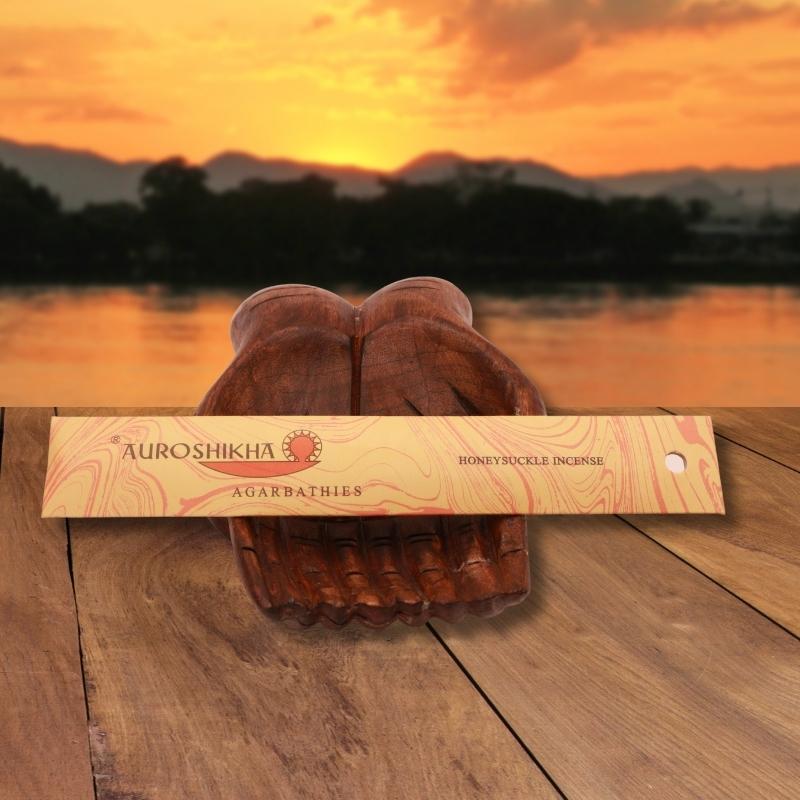 pk of auroshikha incense sitting on a carved wooden hand on a jetty, in front of a golden sunset