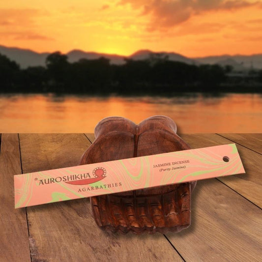 pk of auroshikha incense sitting on a carved wooden hand on a jetty, in front of a golden sunset