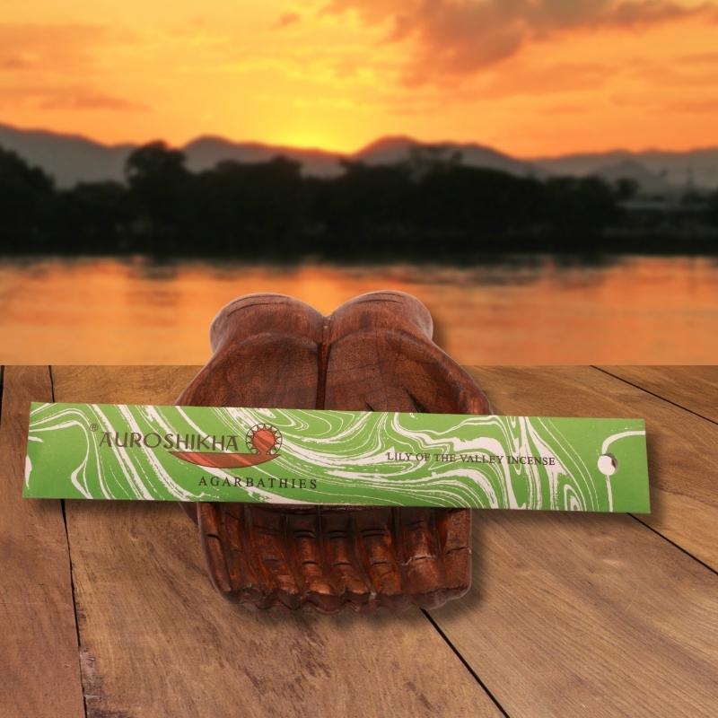 pk of auroshikha incense sitting on a carved wooden hand on a jetty, in front of a golden sunset