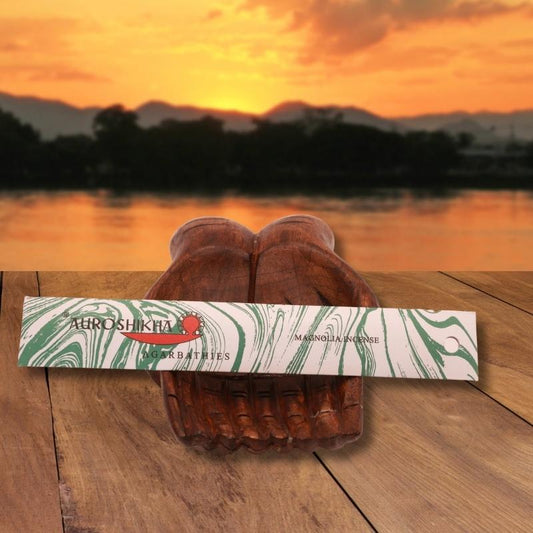 pk of auroshikha incense sitting on a carved wooden hand on a jetty, in front of a golden sunset