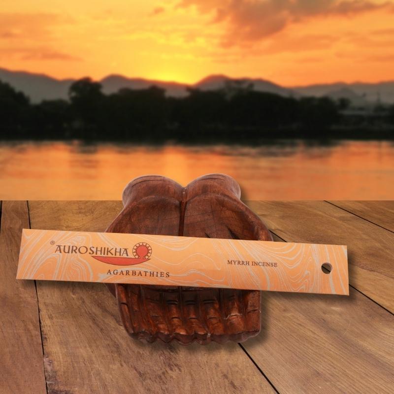 pk of auroshikha incense sitting on a carved wooden hand on a jetty, in front of a golden sunset