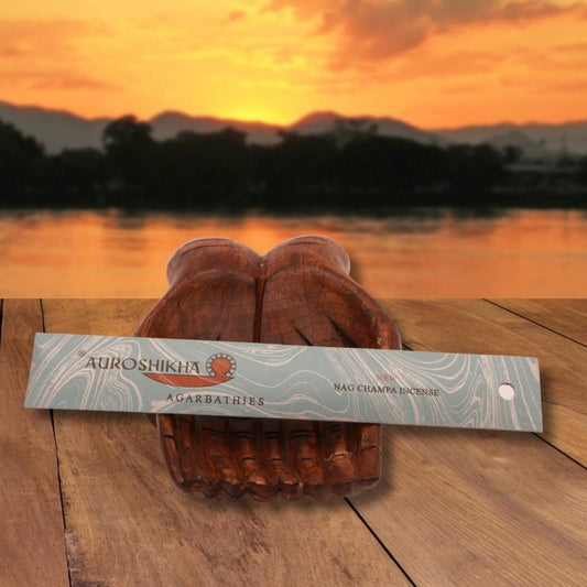 pk of auroshikha incense sitting on a carved wooden hand on a jetty, in front of a golden sunset