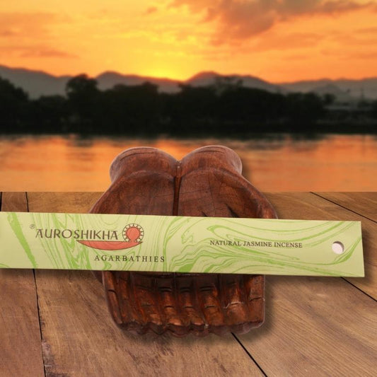 pk of auroshikha incense sitting on a carved wooden hand on a jetty, in front of a golden sunset