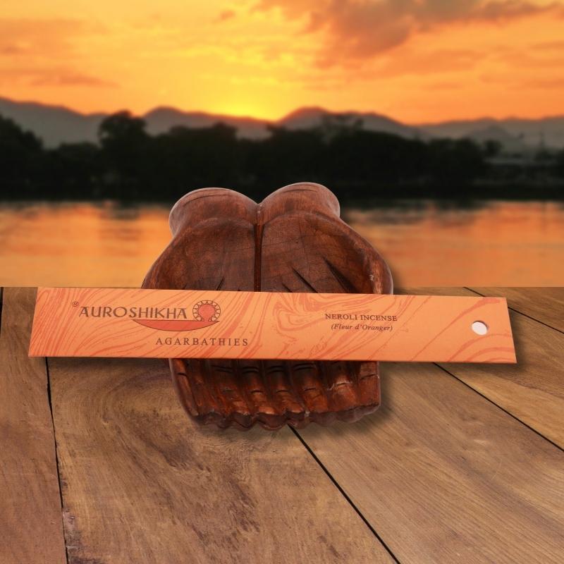 pk of auroshikha incense sitting on a carved wooden hand on a jetty, in front of a golden sunset