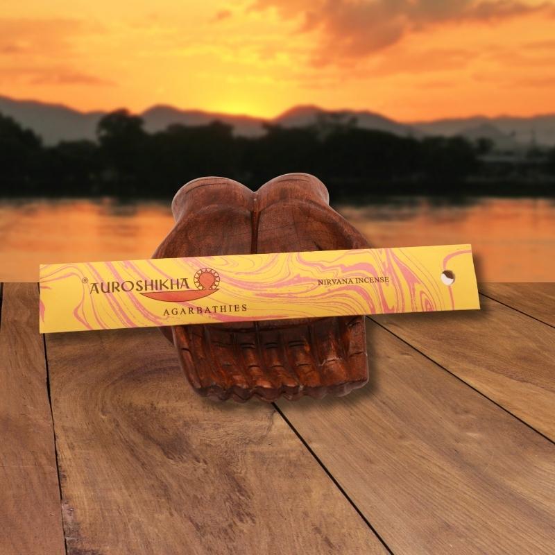 pk of auroshikha incense sitting on a carved wooden hand on a jetty, in front of a golden sunset