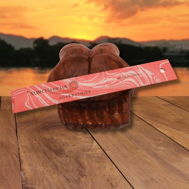 pk of auroshikha incense sitting on a carved wooden hand on a jetty, in front of a golden sunset