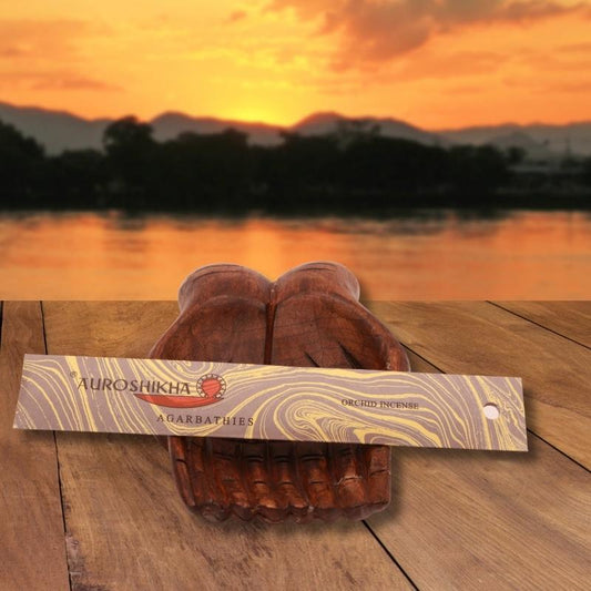 pk of auroshikha incense sitting on a carved wooden hand on a jetty, in front of a golden sunset