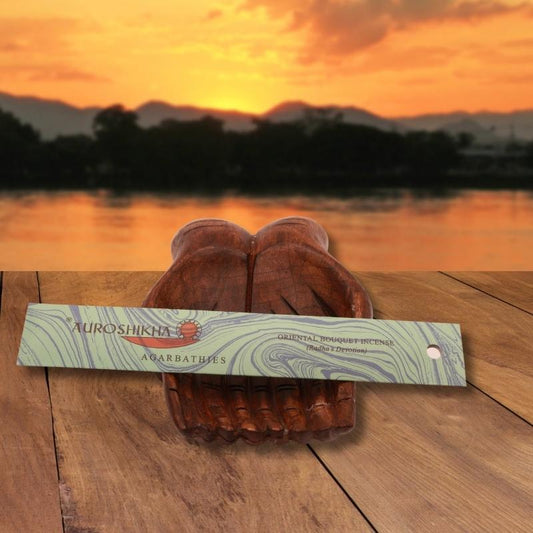 pk of auroshikha incense sitting on a carved wooden hand on a jetty, in front of a golden sunset