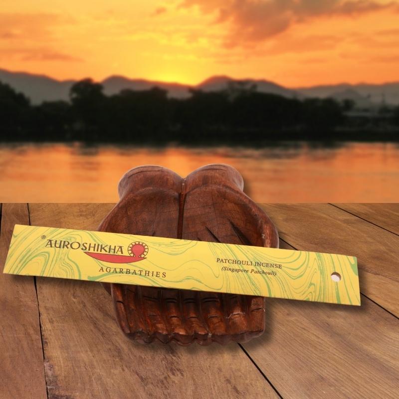 pk of auroshikha incense sitting on a carved wooden hand on a jetty, in front of a golden sunset