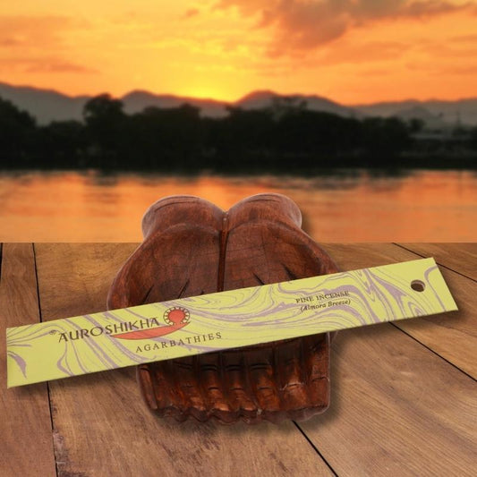 pk of auroshikha incense sitting on a carved wooden hand on a jetty, in front of a golden sunset