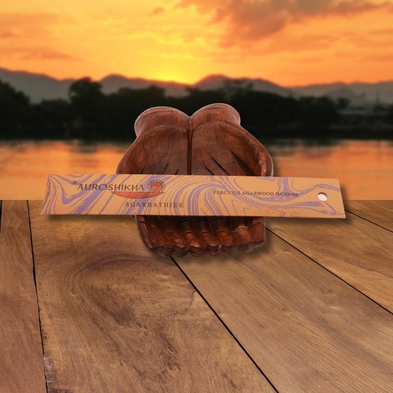 pk of auroshikha incense sitting on a carved wooden hand on a jetty, in front of a golden sunset