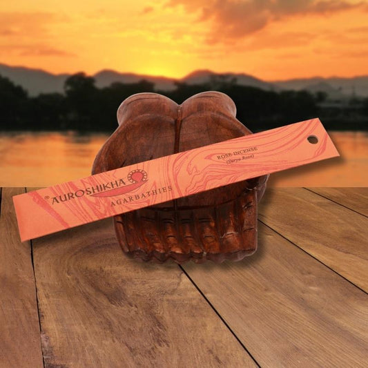 pk of auroshikha incense sitting on a carved wooden hand on a jetty, in front of a golden sunset