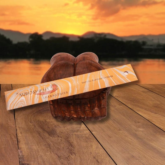 pk of auroshikha incense sitting on a carved wooden hand on a jetty, in front of a golden sunset